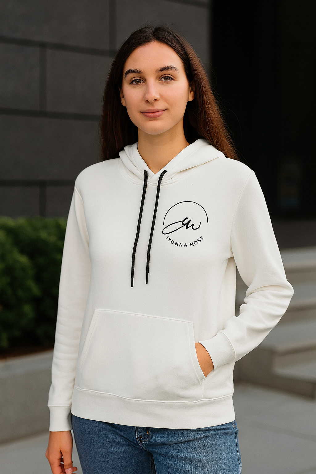 Woman wearing a white hoodie with a logo, standing outdoors.